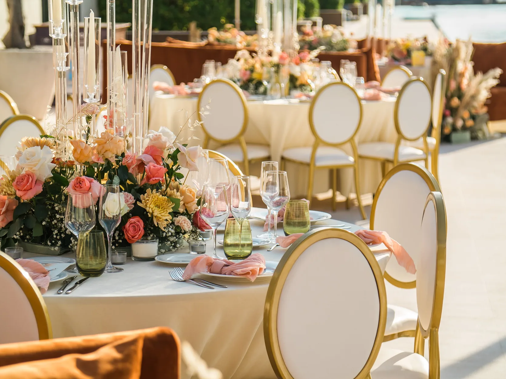 Waterfront reception tables dressed with blush and peach florals and gold cane chairs