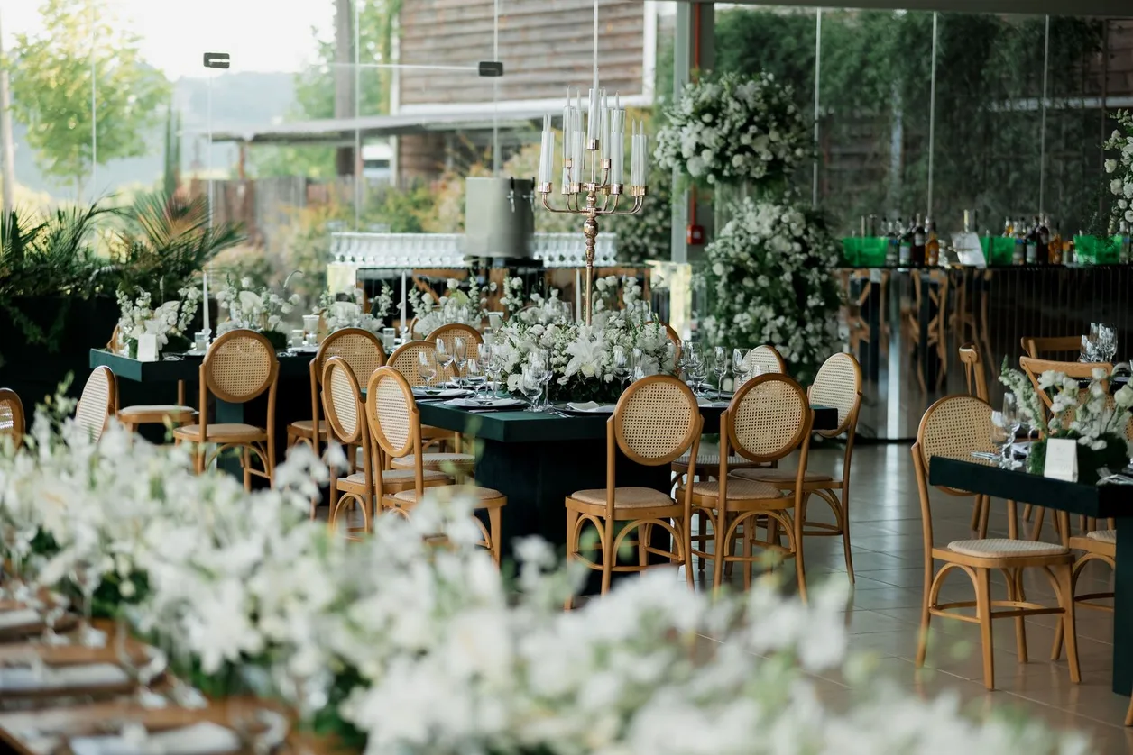 Reception room layered with white blossoms, greenery and cane chairs