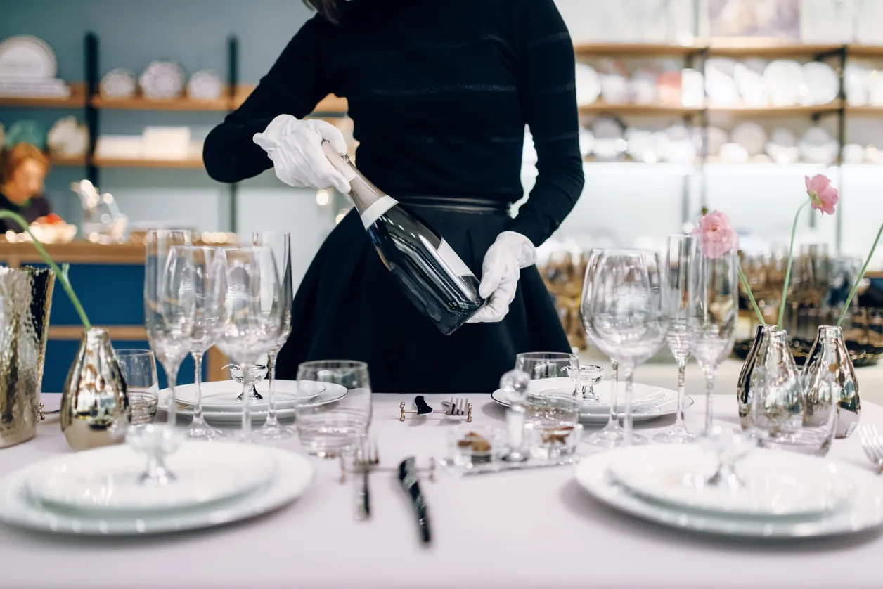 A server pouring wine at a table laid with crystal and white linen