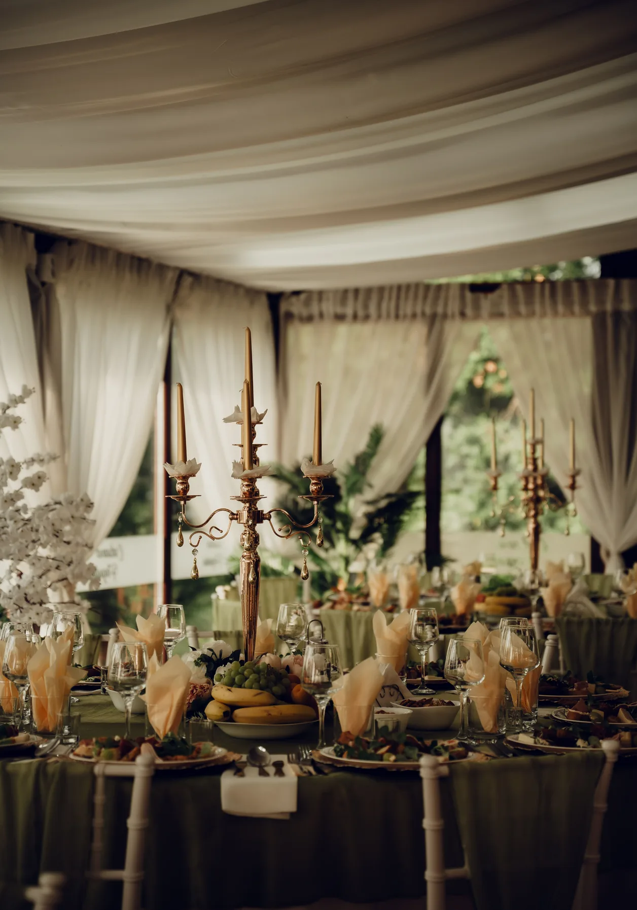 Tented dinner with a draped ceiling, brass candelabra and olive linens