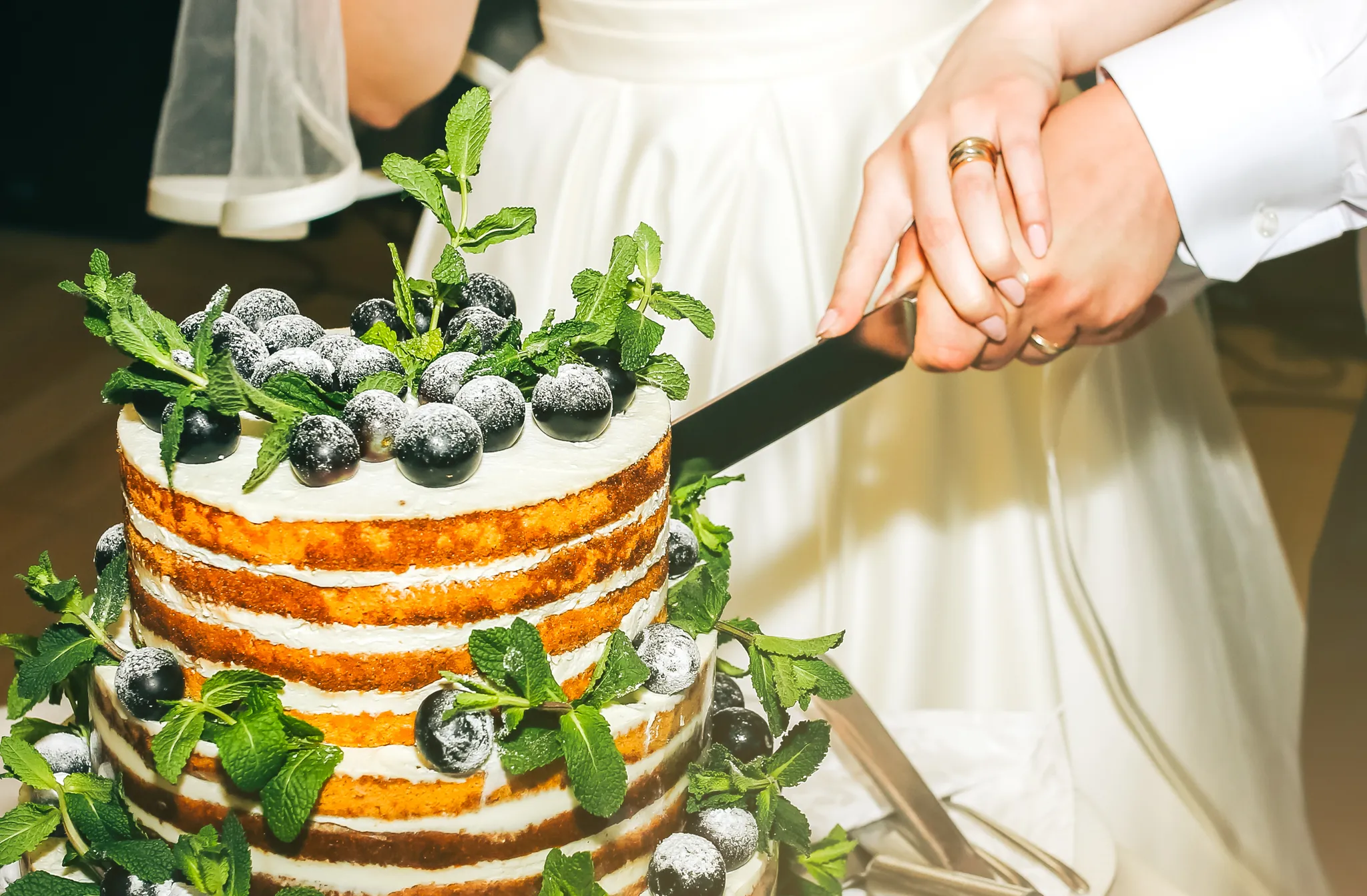 Couple cutting a tiered wedding cake dressed with berries
